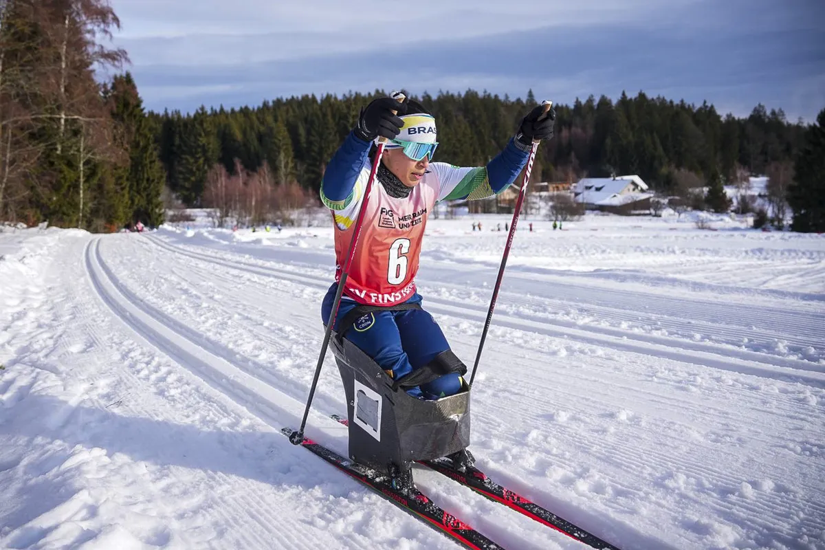 Elena Sena esquiando em uma pista de esqui cross-country durante um dia ensolarado de inverno, com montanhas nevadas ao fundo.