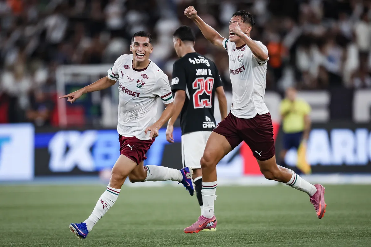 Jogadores do Fluminense comemoram gol em partida contra o Vasco no Nilton Santos, com a torcida ao fundo e luzes do estádio.