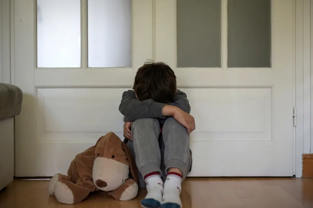 Criança protegendo os olhos, com fundo digital e luzes de polícia, simbolizando a luta contra o abuso sexual infantojuvenil online.