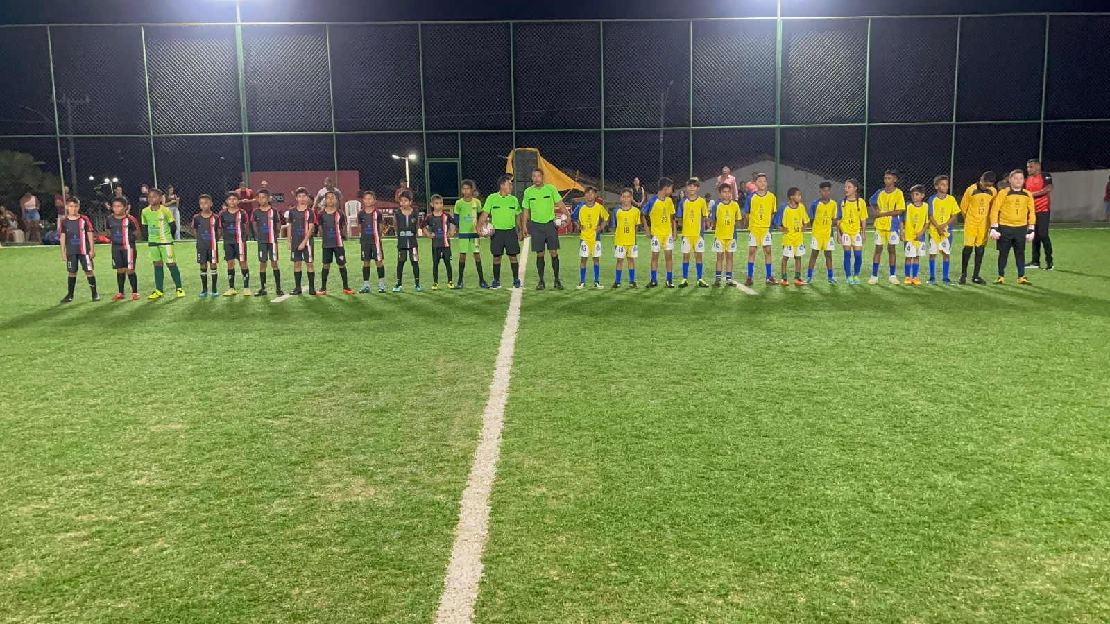 Equipes das escolinhas de futebol de Pequizeiro-TO e Couto Magalhães-TO perfiladas no campo society de Pequizeiro, ao lado de autoridades municipais e regionais, antes do amistoso que terminou em 4 x 1 para o Projeto “Pé na Bola, Cabeça na Escola”.