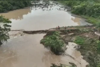 Ponte destruída pela força das chuvas no sudeste do Tocantins, com estrada alagada e vegetação arrancada, causando isolamento de famílias.
