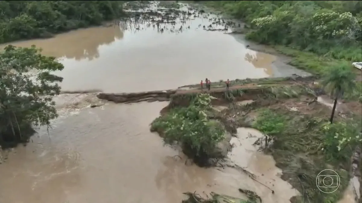 Ponte destruída pela força das chuvas no sudeste do Tocantins, com estrada alagada e vegetação arrancada, causando isolamento de famílias.
