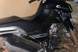 Moto parcialmente queimada estacionada em rua de bairro residencial em Guaraí, Tocantins, cercada por moradores curiosos durante atendimento de ocorrência policial à noite.