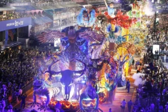 Carro alegórico em desfile de Carnaval no Rio de Janeiro, com imagem de figura política central, em meio à multidão e fantasias, gerando debate.