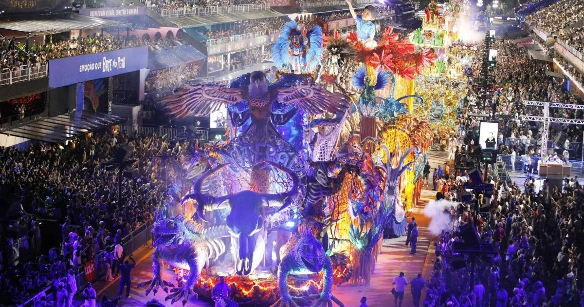 Carro alegórico em desfile de Carnaval no Rio de Janeiro, com imagem de figura política central, em meio à multidão e fantasias, gerando debate.