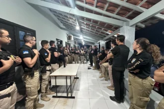 Policiais civis cumprindo mandados em uma operação contra fraude em concurso público, com documentos e algemas visíveis