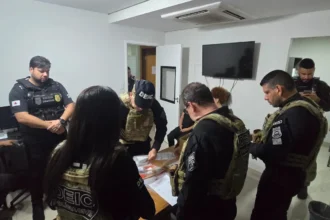 Mão de policial com luva tática segurando tablet com mensagens de ameaça, simbolizando investigação de extorsão online