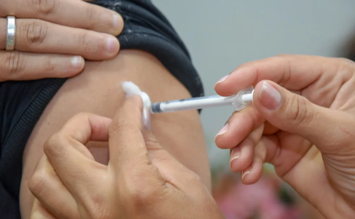 Profissional de saúde aplicando vacina contra a gripe no braço de um adulto em uma unidade de saúde.