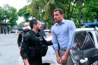 Vereador sendo conduzido por policiais em operação, com favela ao fundo, simbolizando a tensão política no Rio