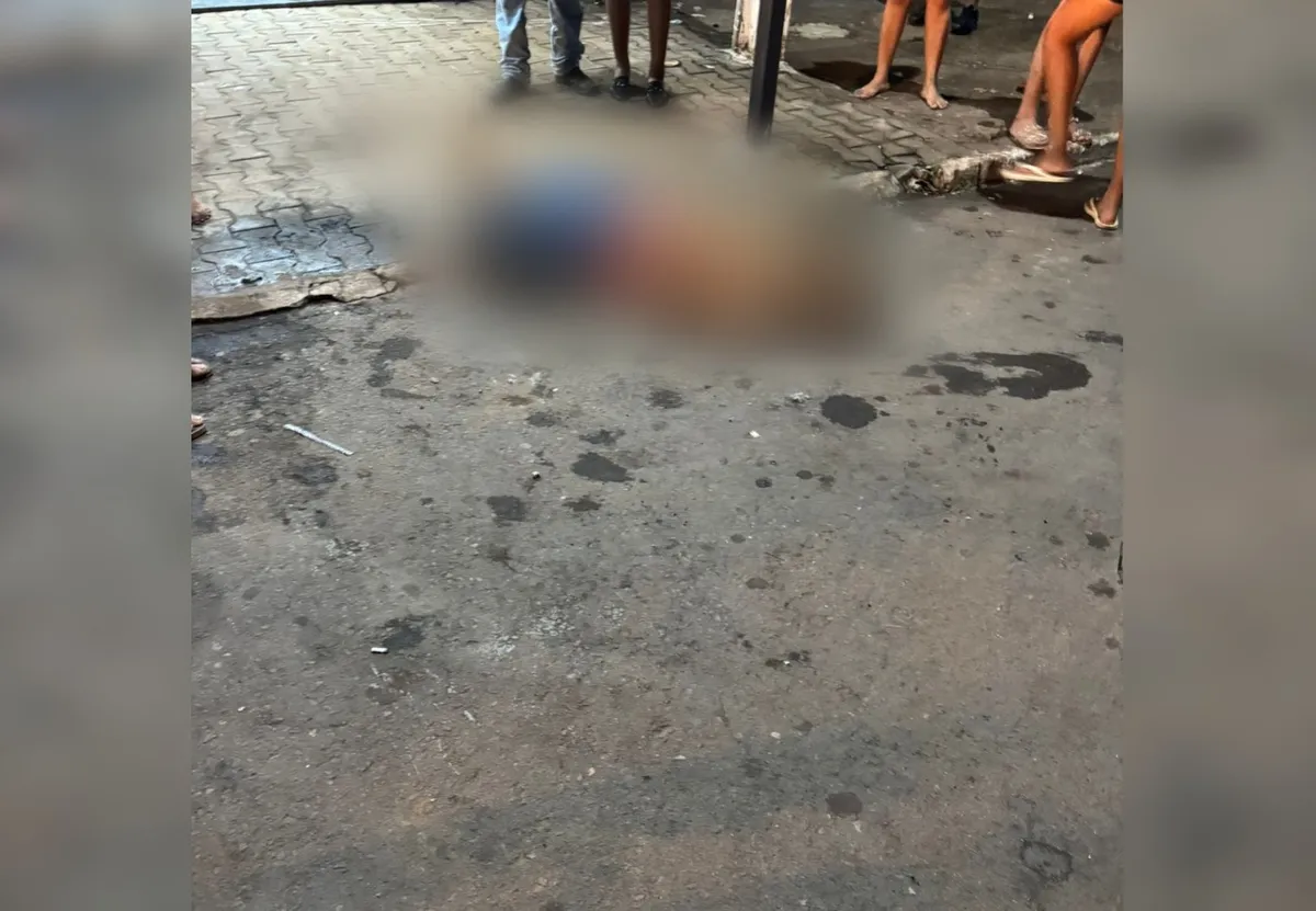 Rua central de Wanderlândia à noite, cena de crime com estabelecimento comercial ao fundo