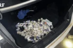 Agente da PRF inspecionando medicamentos e anabolizantes apreendidos em compartimento secreto no porta-malas de um carro na BR-153 em Guaraí.