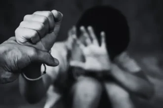 Mãos de adulto protegendo mãos de criança com viaturas policiais e bandeira do Tocantins ao fundo, simbolizando a Operação Caminhos Seguros no Maio Laranja.